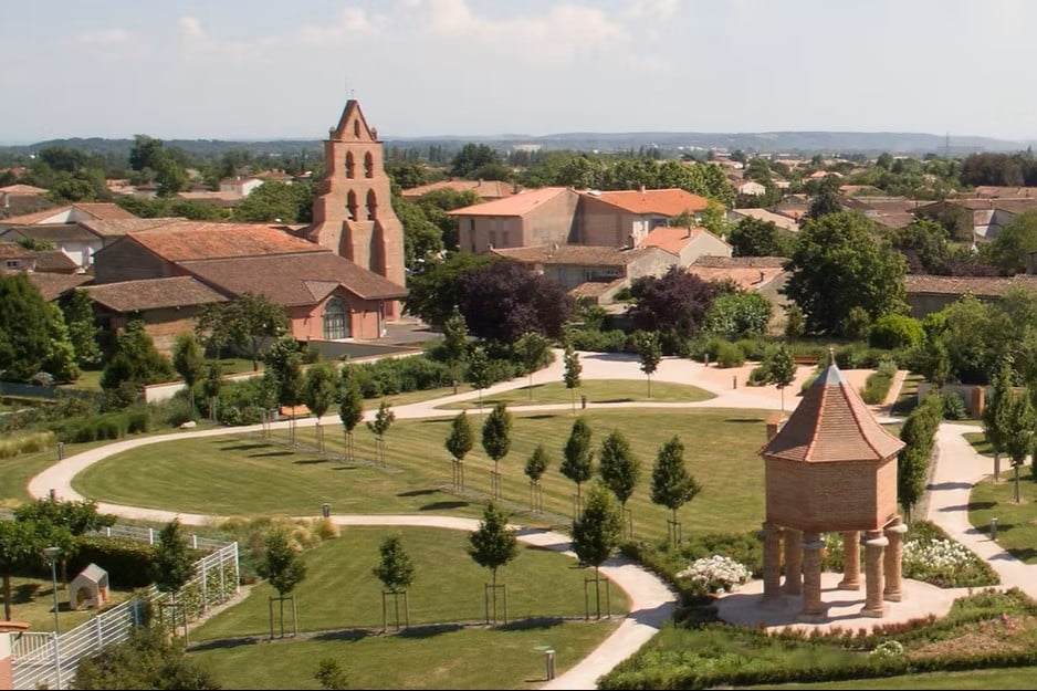 Village du Sud-Ouest : Parc, Pigeonnier et Église en Briques Parc paysager avec pigeonnier et église à clocher-mur en briques rouges dans un village du Sud-Ouest.