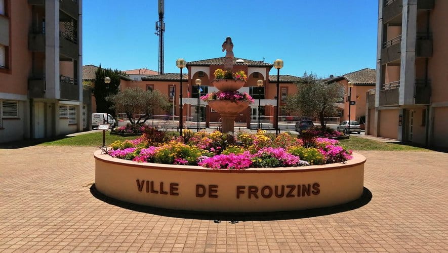 Fontaine et parterre de fleurs coloré marqué Ville de Frouzins sur une place ensoleillée devant la mairie.