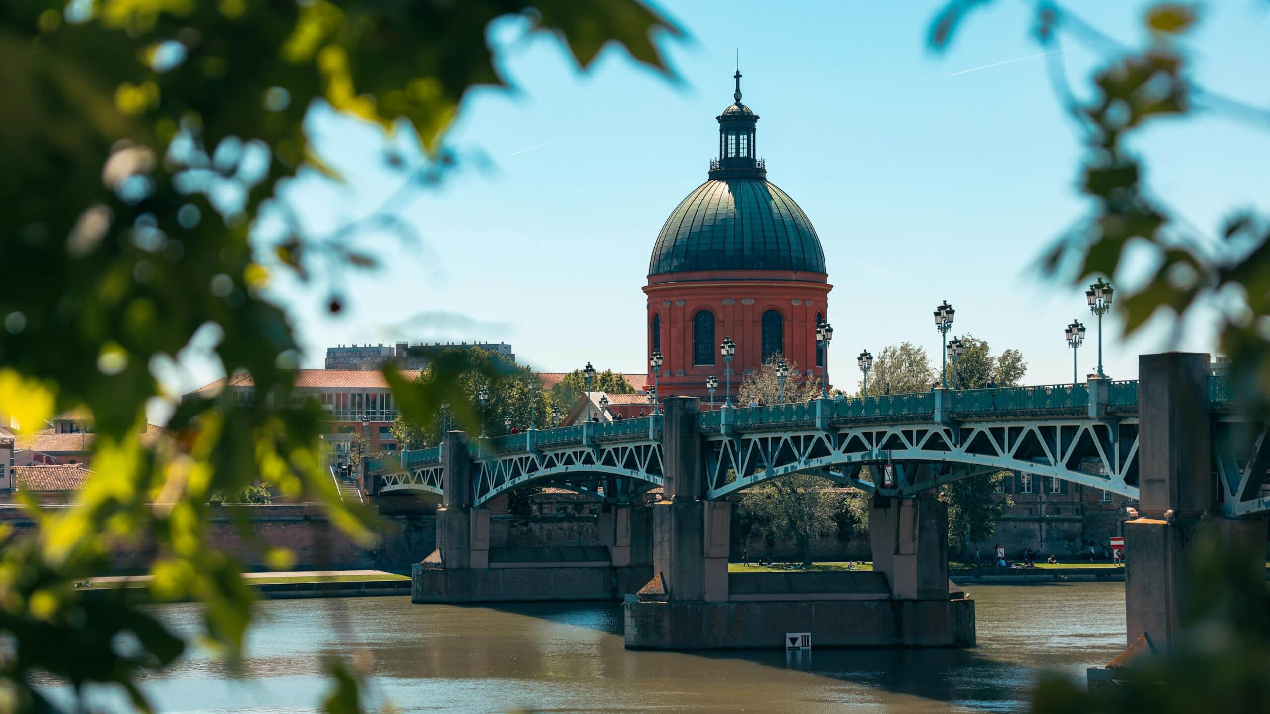 Pont Saint-Pierre et dôme de l'Hôpital de la Grave à Toulouse encadrés de feuilles vertes au-dessus de la Garonne.